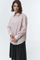 Camisa de algodón y nylon, color rosa pálido con finas rayas verticales blancas. Presenta un cuello clásico, botones frontales y un calce oversized.