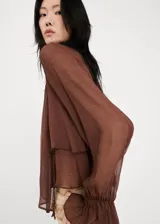 Blusa de viscosa color marrón chocolate, con diseño semitransparente, cuello alto y mangas largas con puños acampanados y volados.