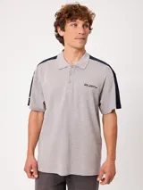 Remera polo gris melange de ajuste holgado, con cuello y cierre frontal de botones. Presenta detalles en azul marino y blanco en los hombros y mangas, y el logo de la marca bordado en el pecho.