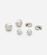 Kit de caravanas femeninas de metal que incluye tres modelos con diseño bold y moderno: dos pares de aretes esféricos de distinto tamaño y un ear cuff de encastre. Cuentan con superficie lisa y acabado pulido.
