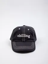 Gorro de béisbol negro con bordado frontal de la palabra "chilling" en blanco y pespuntes blancos en contraste.