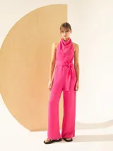 Mono fucsia con escote halter, espalda descubierta, lazo en la cintura y pantalón palazzo con tajos laterales.