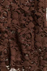 Blusa de manga larga en encaje marrón oscuro con patrón floral. Presenta escote redondo y un borde festoneado en el bajo.
