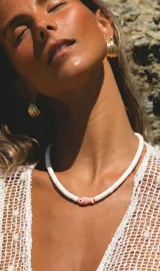 Collar de discos de caracol blancos con un dije central de cerámica en forma de pez rosado con detalles en negro y cierre de acero.
