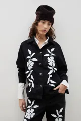 Camisa de denim negro con estampa floral blanca, cuello camisero, cierre frontal con botones y mangas largas.