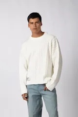 Sweater de punto color blanco con diseño de textura combinada, presentando una mitad lisa y la otra mitad con tejido de trenzas. Posee cuello redondo, corte relajado y una pequeña etiqueta decorativa en el frente.