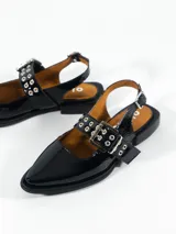 Chatas de cuero negro charol con punta fina, tira sobre el empeine con hebilla y ojalillos metálicos, y tira trasera con hebilla.