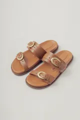 Sandalias planas de cuero negro con diseño de dos tiras ajustables con hebillas metálicas.