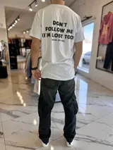 Remera blanca de manga corta con estampa frontal y de texto grande en la espalda que dice 'DON'T FOLLOW ME (I'M LOST TOO)' y la marca 'DUXON ORIGINAL'.