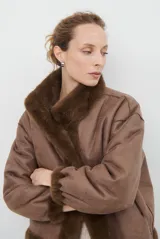 Chaqueta de piel sintética en color burdeos, con cuello alto y cierre frontal oculto. Presenta un diseño de corte recto y mangas largas con puños ligeramente ajustados.