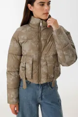 Campera puffer corta color verde con estampado difuminado, cierre frontal con cremallera, cuello alto y bolsillos con solapa y hebilla.