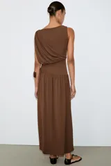 Vestido largo sin mangas de cuello redondo, confeccionado en tejido drapeado con detalle de cintura tipo fajín en el mismo material.