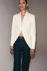 Blazer tipo frac de corte largo y diseño sin solapa. Presenta mangas largas con abertura, falsos bolsillos de vivo en el delantero y bajo asimétrico. Cuenta con cierre frontal mediante gancho metálico y forro interior a tono.