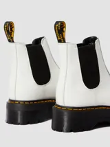 Botas Chelsea de plataforma Dr. Martens modelo 2976 Quad, confeccionadas en cuero liso color blanco. Presentan paneles elásticos laterales en color negro, suela de plataforma dentada tipo comando con costuras amarillas características y tirador trasero con logo de la marca.