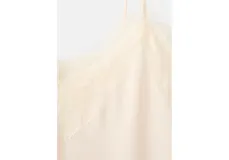 Top de satén color crema con escote en V y detalle de puntilla en el borde inferior. Presenta breteles finos y un corte fluido.