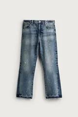 Jeans flare fit de hombre confeccionados en denim de algodón color azul con efecto lavado y roturas. Presentan diseño de cinco bolsillos, efecto salpicaduras de pintura en toda la prenda y bajo con acabado irregular.