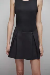 Vestido negro sin mangas, con escote redondo y falda corta plisada.