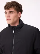Campera reversible de nylon con cuello alto y cierre frontal. Un lado es de color gris liso con logo bordado, mientras que el otro lado presenta un estampado abstracto en tonos azules. Cuenta con bolsillos laterales y puños elásticos.