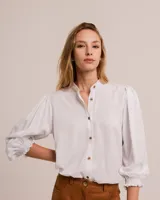 Blusa celeste de cuello mao y mangas abullonadas con puños elásticos. Tiene tajos laterales y botones en la delantera.