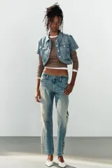 Jeans rectos de tiro medio en denim azul con efecto deslavado. Presentan bandas laterales con detalles brillantes, bolsillos delanteros y traseros, y aberturas en los tobillos con botonadura metálica.