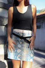 Minifalda con estampado de piel de serpiente en tonos celeste y blanco, con pretina ancha color crudo y cinturón fino negro.