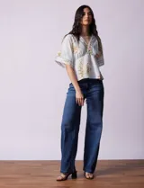 Blusa blanca estampada con flores azules, escote en V y mangas cortas amplias. Detalles de puntilla en escote y mangas.