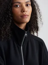 Campera negra de corte holgado con cierre bidireccional, cuello alto y bolsillos frontales.