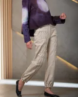 Pantalón babucha color beige de algodón, con corte a la cintura y piernas levemente amplias. Presenta textura de tablitas centrales y elásticos con broches inferiores que ajustan las piernas al tobillo.