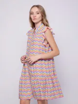 Vestido corto con estampado floral multicolor, cuello tipo camisa y cierre frontal con botones. Presenta volados en las sisas y un diseño de falda con volados en el ruedo.