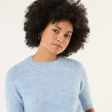Sweater de punto de textura suave, color azul claro, con cuello redondo y mangas cortas. Presenta un diseño de corte recto con terminaciones acanaladas en cuello, mangas y ruedo.