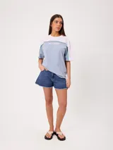 Remera oversize de manga corta marca Rusty, modelo Rocca, en combinación de colores celeste, blanco y detalles en verde. Presenta estampado frontal con el logo de la marca y diseño de bloques de color.