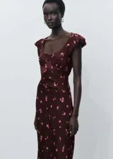 Vestido midi de color bordó con estampado de flores rosas, presenta un diseño entallado con cuello escotado y mangas cortas abullonadas, incluye cierre de cremallera lateral y abertura en la espalda.