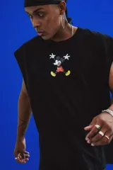 Sudadera sin mangas negra de calce oversize, confeccionada en algodón premium. Presenta un estampado grande en la espalda con la cara de Mickey Mouse usando auriculares, rodeado de elementos gráficos de equipos de música y luces de neón.