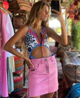 Minifalda de tiro bajo color rosa, estilo jean, con costuras visibles y tajo lateral. Presenta un botón metálico en el frente y un pequeño parche de marca en el bolsillo delantero.