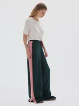 Pantalón tejido de corte amplio y tiro alto, color verde oscuro con franja lateral vertical en color rosado con diseño de trenzas. Presenta cintura elástica con cordón de ajuste y tajos laterales en el ruedo.