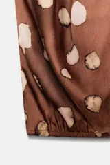 Top de cuello subido y diseño sin mangas, confeccionado en tejido satinado con estampado de manchas abstractas. Presenta drapeado frontal, bajo con elástico y cierre posterior con botones.