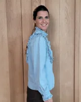 Camisa de denim negro con cuello alto, cierre frontal de botones y detalles de volados en el frente y puños.