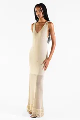 Vestido largo de punto abierto con sutil brillo dorado, escote en V y diseño sin mangas con detalles de flecos en el ruedo.