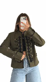 Campera estilo militar color verde oliva, con ribetes negros, cuello mao y detalles de pasamanería trenzada negra en el frente. Cuenta con botones metálicos y puños anchos con botones y ribete negro.