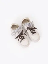 Zapatillas de cuero vacuno en color beige, con recortes de gamuza en la puntera y talón, doble cordón en tonos gris y marrón, hebilla lateral y dije colgante en la cordonera. Suela plana de goma.