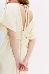 Vestido largo color crema, con escote en V en el frente y espalda. Presenta mangas cortas amplias, talle ajustado con lazo trenzado y tajos laterales.