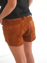 Shorts de cuero color marrón tostado, con volados frontales decorativos en los laterales, trabillas para cinto y cierre de botón frontal.