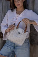 Cartera tipo mini bag de cuero con acabado texturizado en color beige claro, con manijas cortas de cuero marrón y cierre frontal metálico tipo torniquete.
