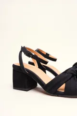 Sandalia de tacón cuadrado medio, confeccionada en terciopelo negro. Presenta un diseño de tiras cruzadas con nudo en la parte delantera y una tira ajustable con hebilla en el tobillo.