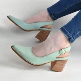 Zapatos stiletto destalonados de cuero color verde menta, con taco ancho de madera y hebilla metálica dorada de ajuste en el talón. Presentan punta fina y costuras visibles en el borde de la suela.