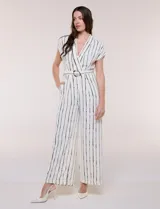 Enterito largo ABS Allen Schwartz de calce fluido, color blanco con diseño de rayas verticales negras. Presenta escote en V cruzado, mangas cortas, cintura definida con cinturón y hebilla ovalada, pantalón wide leg con bolsillos laterales y pinzas.