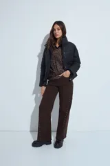 Pantalón de denim corte wide leg color marrón, con ruedo desflecado y detalle de tachas metálicas a lo largo de las costuras laterales.