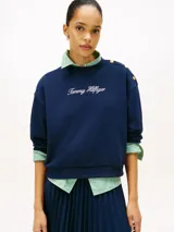 Buzo de felpa Tommy Hilfiger color azul marino, de corte regular y manga larga, con cuello redondo y puños y bajo en punto canalé. Presenta detalle de botones dorados decorativos en el hombro y logotipo de la marca bordado en tipografía script en el pecho.
