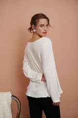 Blusa blanca de manga larga con puntilla de flores en el escote y volado en el ruedo.