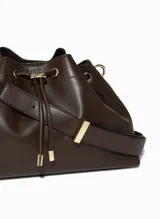 Cartera tipo cubo de Le Lis Blanc, color chocolate, con cierre superior mediante cordón ajustable y herrajes metálicos dorados. Cuenta con una correa larga ajustable para llevar al hombro o cruzada.